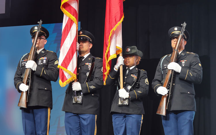 Four military personnel are standing and presenting the American flag and the Texas flag.